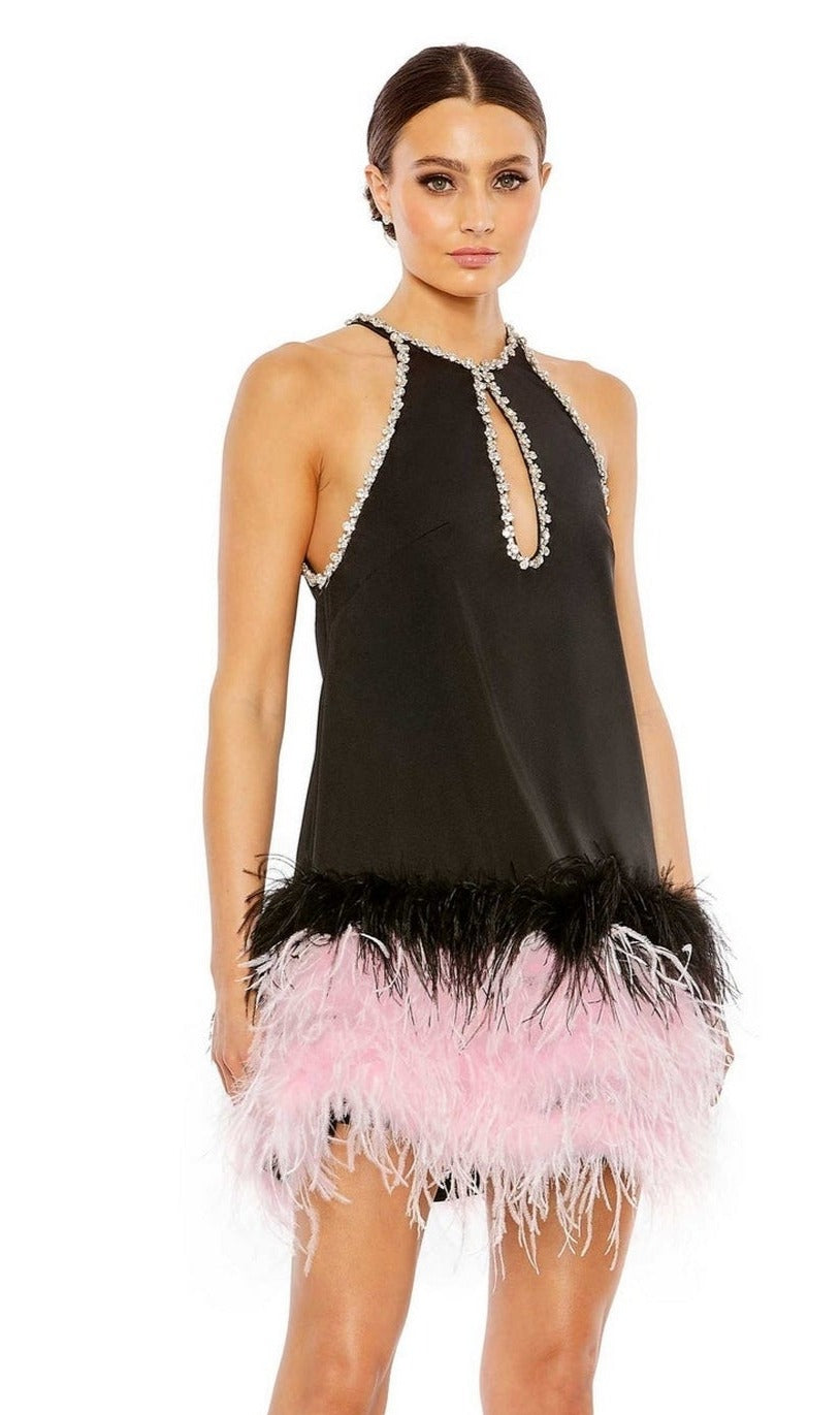 A woman stands against a white background wearing the Short Homecoming Dress 11437 by Mac Duggal—a sleeveless black dress featuring a keyhole cutout neckline, beaded trim, and a black and pink feathered hem.